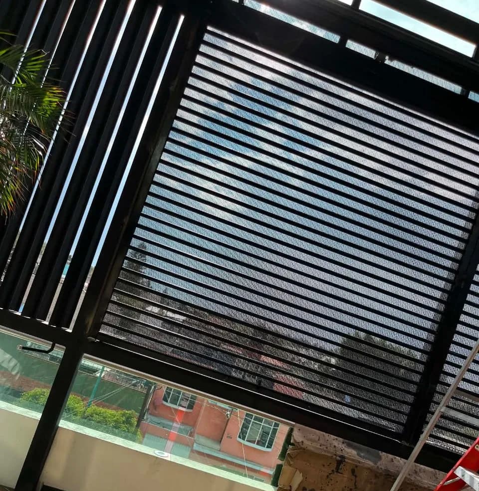 Cortina perforada negra vista desde el interior de una terraza, con el exterior visible a través de la lámina