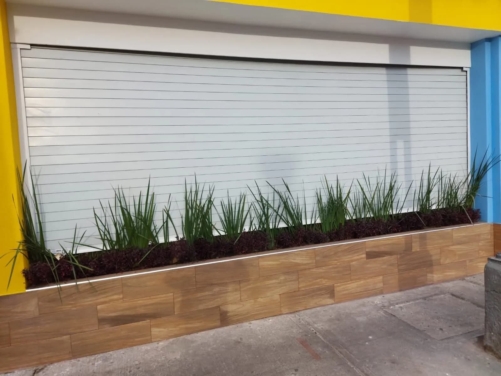 Cortina plana blanca cerrada en la fachada de un local comercial, con jardinera al frente