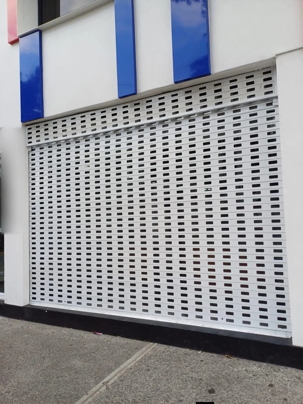 Cortina troquelada blanca con perforaciones rectangulares en la fachada de un local comercial